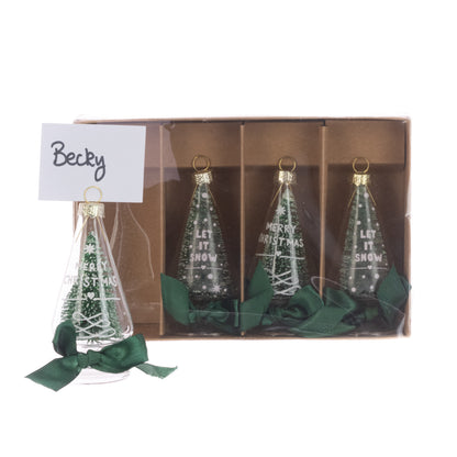 Three clear Christmas tree ornaments with gold rings and green ribbons are shown in a brown gift box, with one ornament outside the box tied with a green bow and a handwritten note that says 'Becky'.