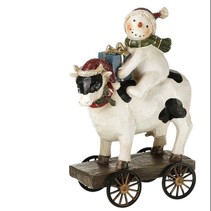 Decorative figurine of a snowman riding a cow on a cart on a white background