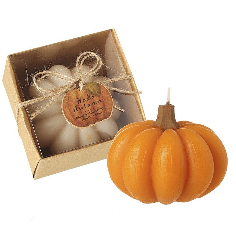 An orange pumpkin-shaped candle shown next to its kraft paper gift box with a clear window, twine bow, and a round tag that reads 'Hello Autumn'.