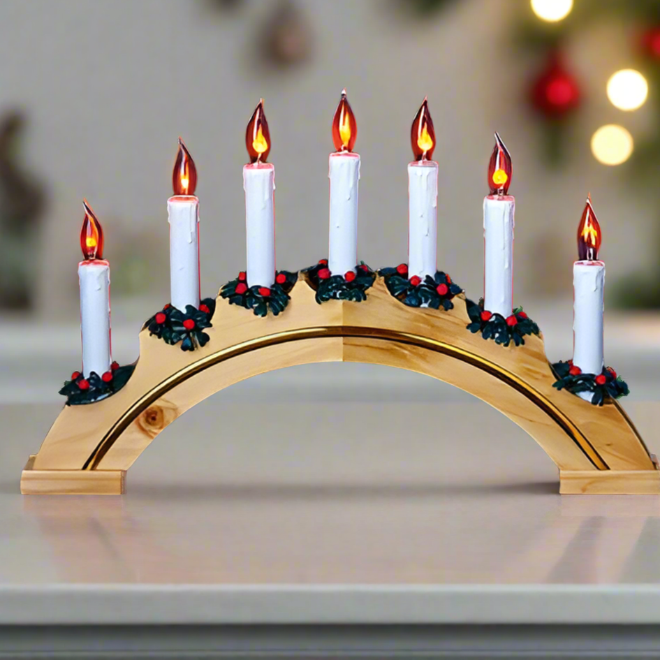 A decorative candle bridge with a pine arch, featuring seven hanging candles with flame-shaped bulbs, adorned with festive foliage and red berries on a table.