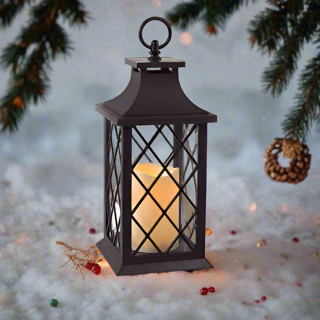 A vintage-style lantern with a flickering candle, primarily black in color, placed on snow-covered ground with Christmas decorations around.