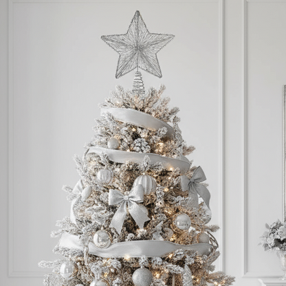 Decorated Christmas tree with white ribbons, ornaments, and a star topper against a white wall.