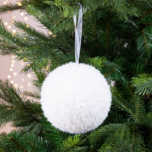 A white round Christmas bauble hanging from a tree with lights and organza ribbons.