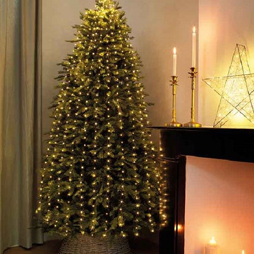 Christmas tree decorated with warm white LED lights with green cable, placed in a room with a fireplace and candles.
