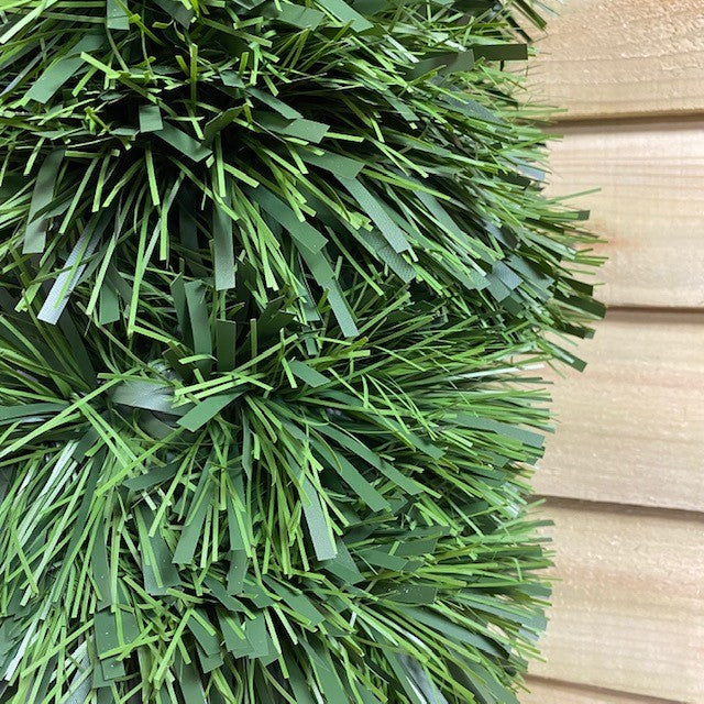 A close-up of a green tinsel Christmas garland with matte finish and a mix of dark and light green foliage.