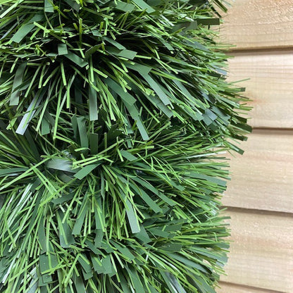 A close-up of a green tinsel Christmas garland with matte finish and a mix of dark and light green foliage.