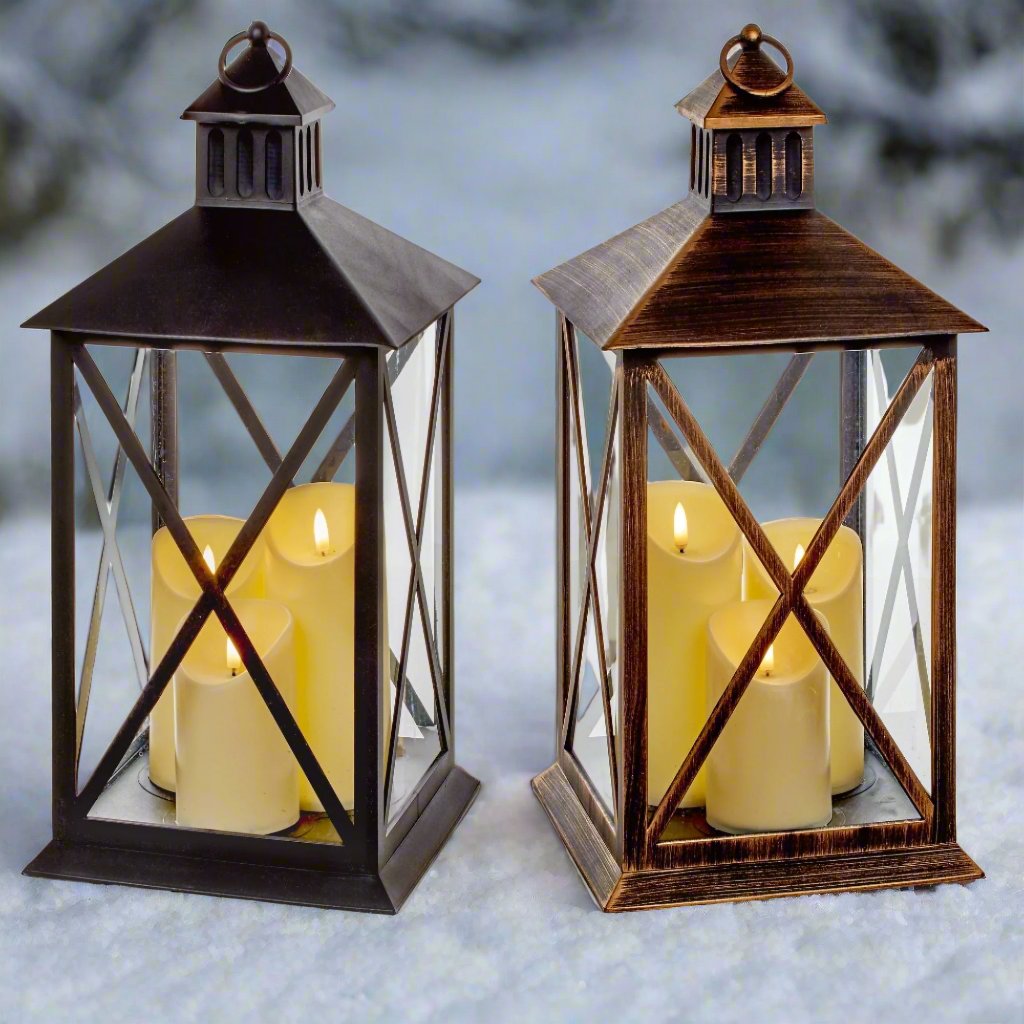 Two cylindrical Christmas lanterns with glass windows and wooden frames. Each lantern contains three candles with a warm white glow, set on a wooden surface.