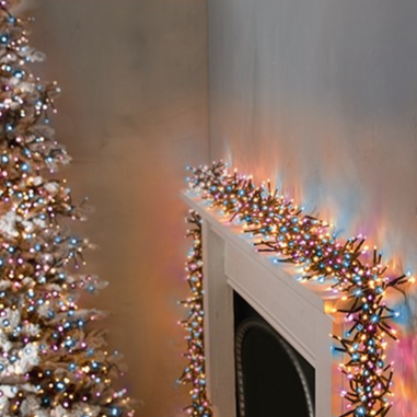 A cluster of LED Christmas lights with a multicolor glow wrapped around a fireplace mantle, with a Christmas tree in the background.