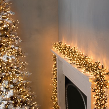 Cluster of Premier 2000 LED Vintage Gold Christmas lights wrapped around a fireplace mantle, with a Christmas tree in the background.