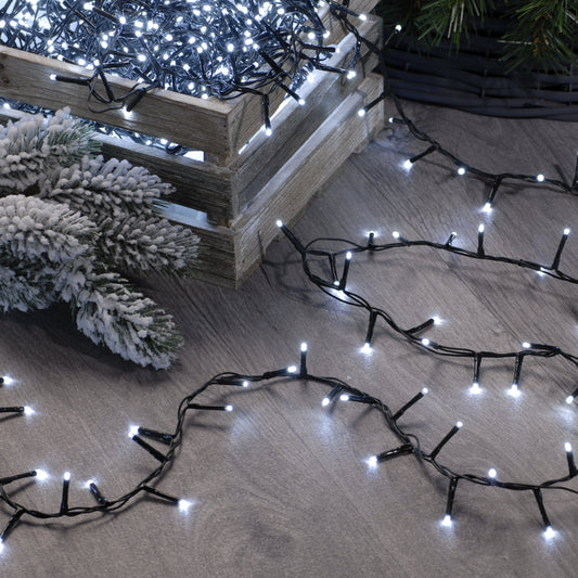 A string of cold white festive sparkle lights placed on a wooden surface with a small tree and decorative branches nearby.