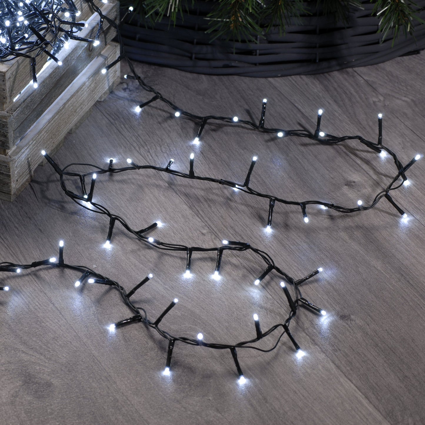 A set of festive sparkle Christmas lights arranged on a wooden floor, designed to illuminate a Christmas tree, with a focus on the lights' glow and not the lights themselves.