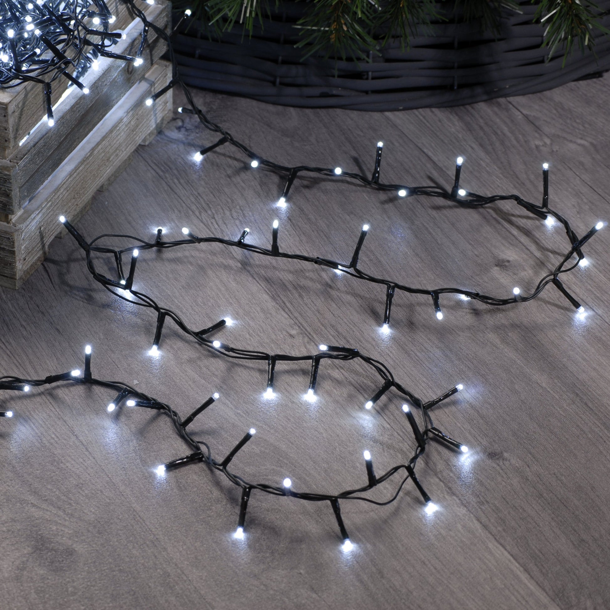A set of festive sparkle Christmas lights arranged on a wooden floor, designed to illuminate a Christmas tree, with a focus on the lights' glow and not the lights themselves.