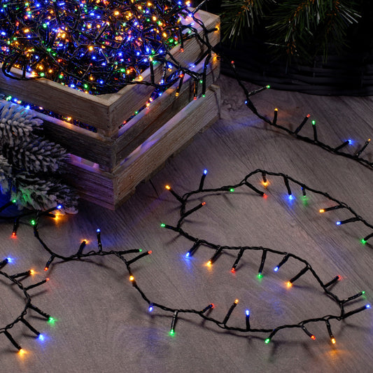 A set of multicolored Christmas lights placed on a wooden surface with a pine tree in the background, and a collection of lights laid out on the floor in front.