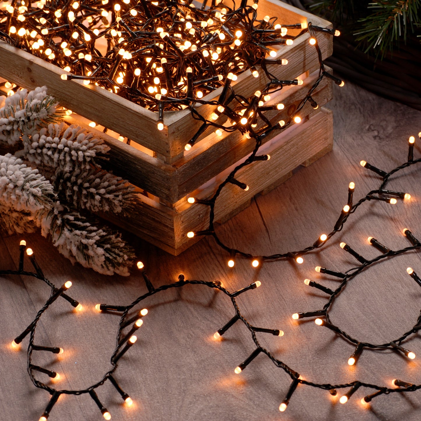 A set of warm white glow worm Christmas lights placed on a wooden surface with pine cones and decorative branches around, creating a festive atmosphere.