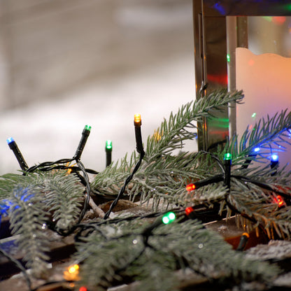 String lights with multicolored LED bulbs, arranged in a festive pattern around a Christmas tree and indoor decorations, with a blurred background of snow and more lights.