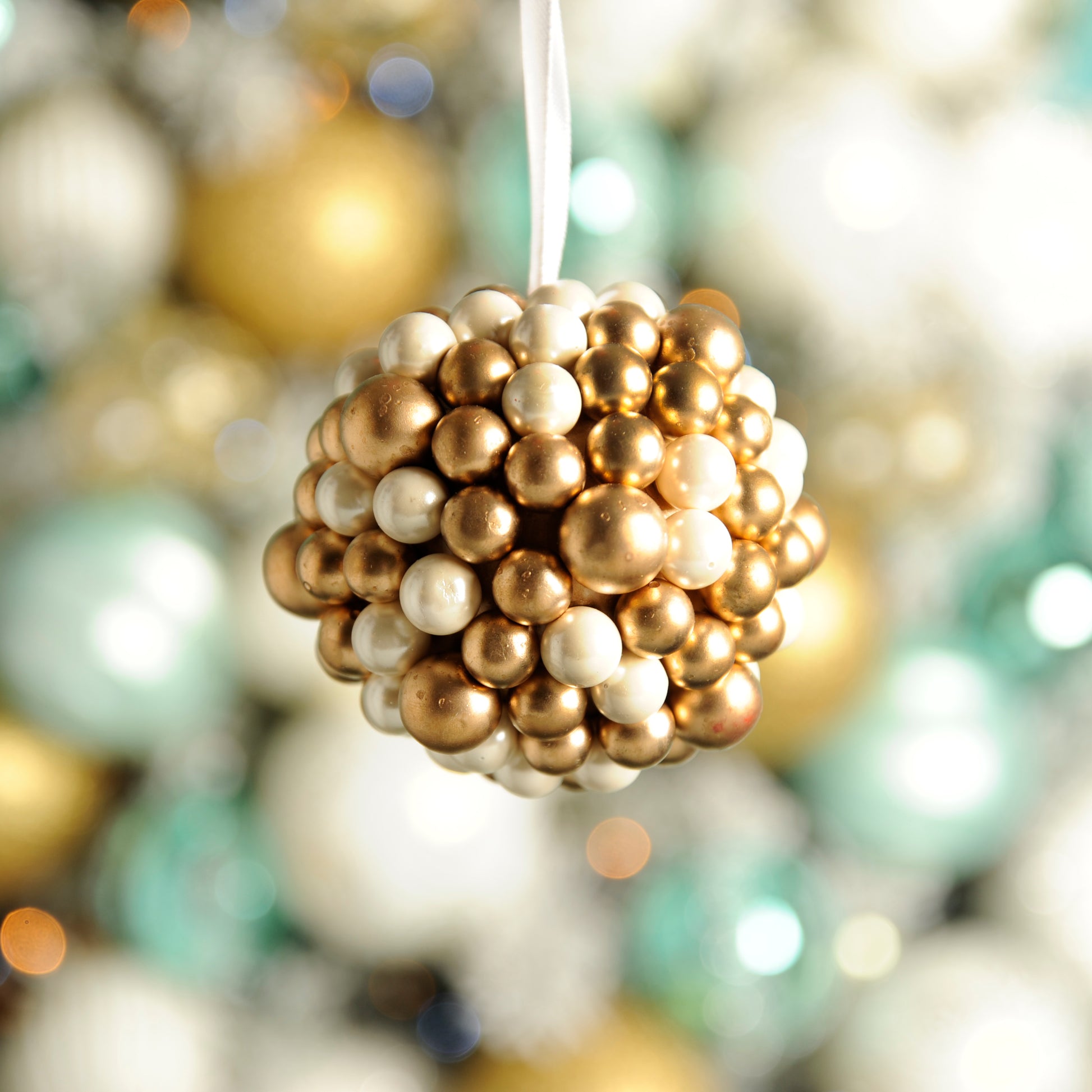 A gold and white berry cluster ball Christmas decoration with a textured surface, surrounded by various colored Christmas balls.