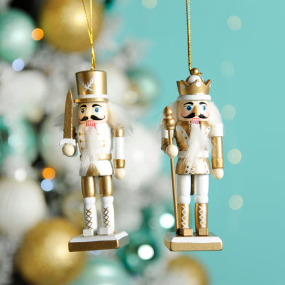 A pair of white and gold nutcrackers hanging from a Christmas tree, one holding a golden staff, the other with a set of balls and a sword.