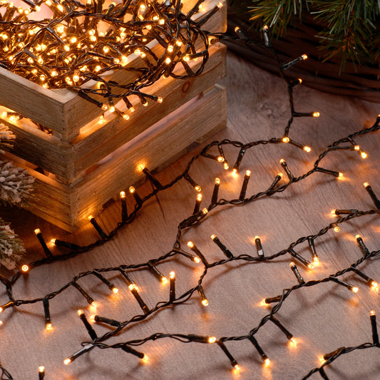 String of warm white Christmas lights placed on a wooden surface with a pine branch and green cable, indoors.
