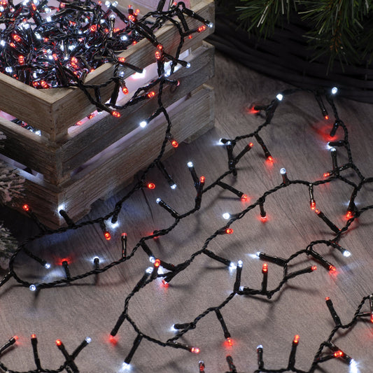A string of red and white Christmas lights displayed on a wooden surface with a green Christmas tree in the background.