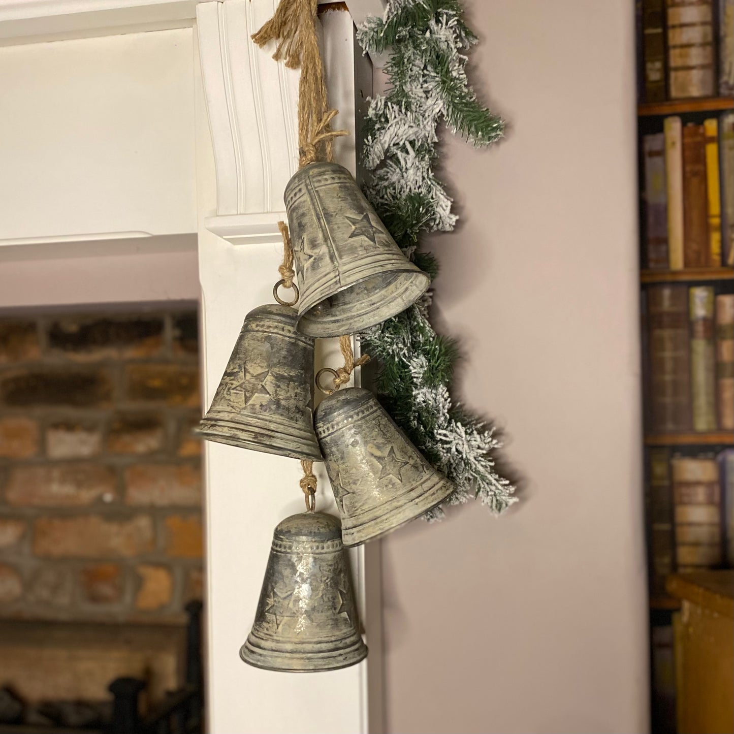 A set of vintage style hanging metal Christmas bells with a jute rope, embossed with a star pattern, displayed indoors.