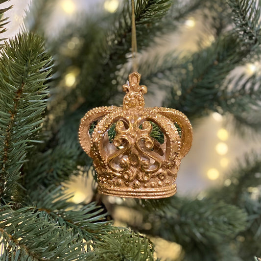 A golden hanging Christmas tree decoration in the shape of a crown, set against a blurred background of Christmas lights.